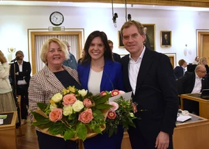 Drei Menschen im Kieler Rathaus, davon zwei mit Blumensträußen in der Hand