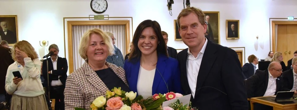 Drei Menschen im Kieler Rathaus, davon zwei mit Blumensträußen in der Hand