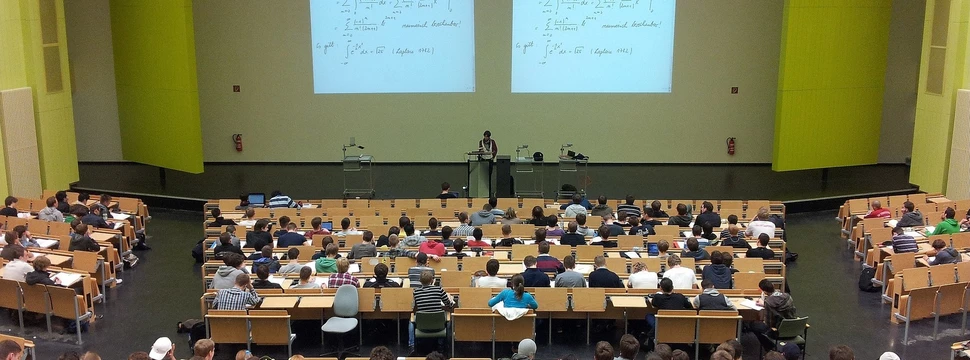 Vorlesungssaal mit Studierenden und Dozent, an der Wand eine Präsentation