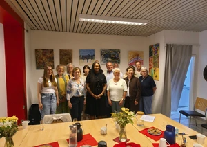 Mehrere Menschen vor einer weißen Wand, an der mehrere Bilder aufgehangen sind und die für ein Foto posieren