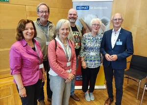 Mehrere Menschen vor einer hölzernen Wand, die vor einem Banner stehen