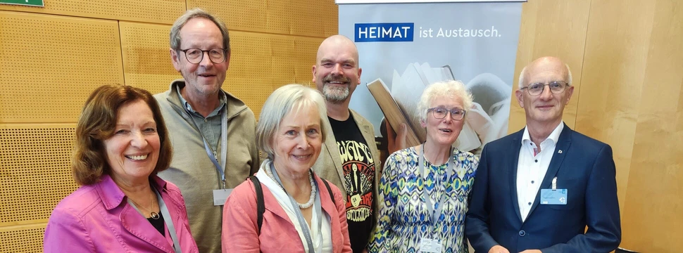 Mehrere Menschen vor einer hölzernen Wand, die vor einem Banner stehen