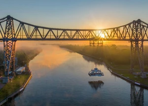 Eine metallerne Brücke in Rensburg über dem Nord-Ostsee-Kanal mit der Schwebefähre an der Unterseite und dem Sonnenuntergang im Hintergrund