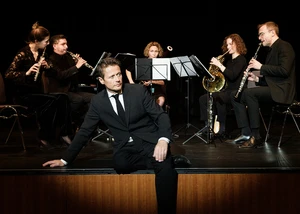 Mehrere Menschen auf einer Bühne, bei denen einige ein Instrument spielen und ein Mensch im Vordergrund sitzt