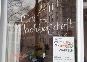 Eine Scheibe eines Hauses am Kieler Südfriedhof, an der "Ort der Nachbarschaft" geschrieben steht