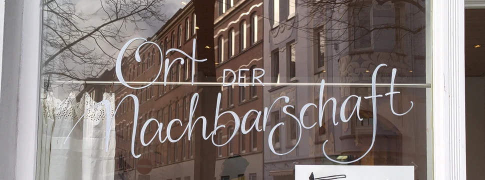 Eine Scheibe eines Hauses am Kieler Südfriedhof, an der "Ort der Nachbarschaft" geschrieben steht