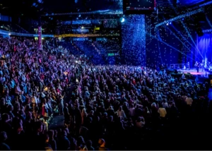 Mehrere hundert Menschen, die gemeinsam in einer Halle im Scheinwerferlicht singen und Spaß haben