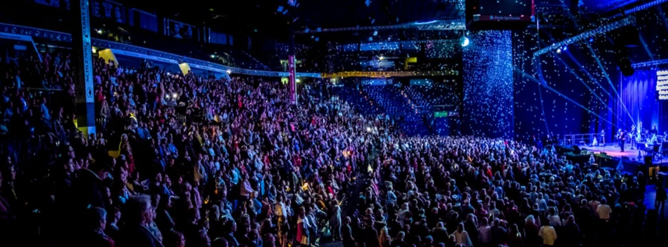 Mehrere hundert Menschen, die gemeinsam in einer Halle im Scheinwerferlicht singen und Spaß haben