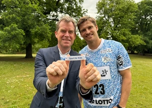 Zwei Männer halten ein weißes Armband in die Kamera
