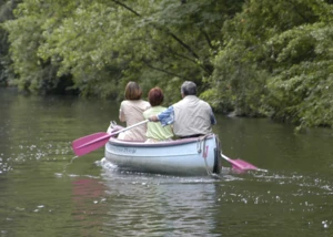 Drei Menschen beim Paddeln auf einem ruhigen Fluss inmitten grüner Natur. Drei Personen paddeln in einem Boot auf einem grünen, von Bäumen gesäumten Fluss.