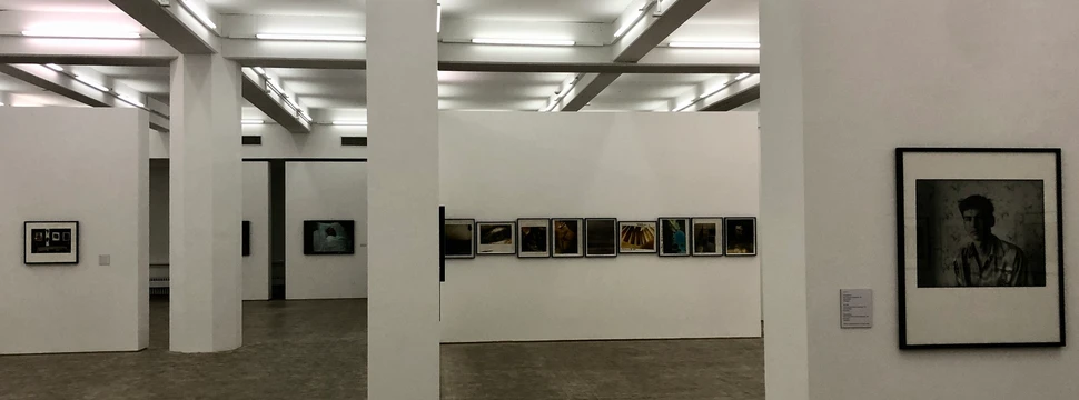 Innenansicht einer modernen Galerie mit Fotografien und Kunstwerken an weißen Wänden.