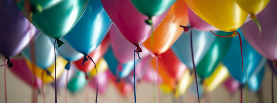 Bunte Luftballons schweben, an ihnen hängt ein Band