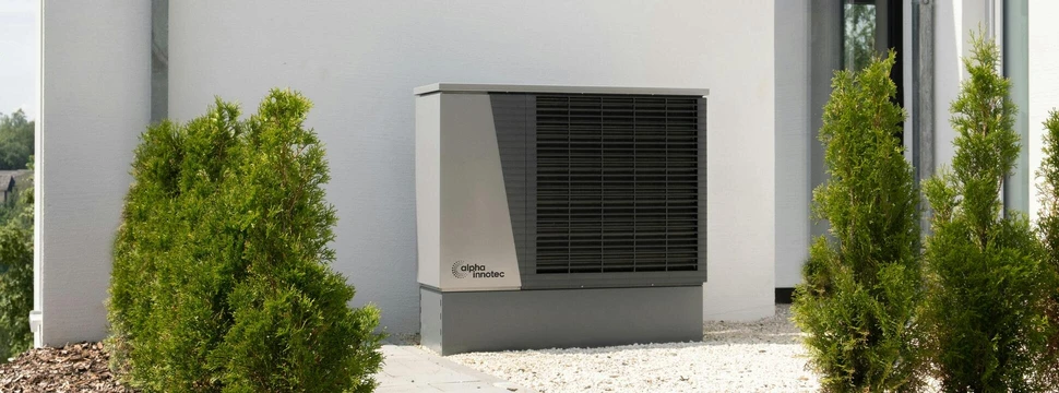 Eine graue Wärmepumpe vor einem Gebäude mit weißen Wänden