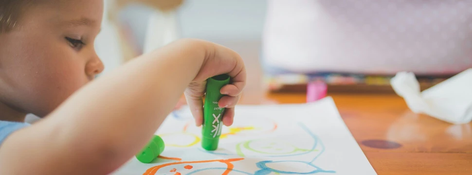 Kind malt mit Wachsmalstiften auf ein Papier