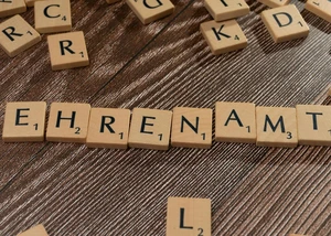Mehrere Buchstaben, die sich auf Holzplättchen auf einem Tisch liegend befinden, und die zusammen das Wort "Ehrenamt" erheben