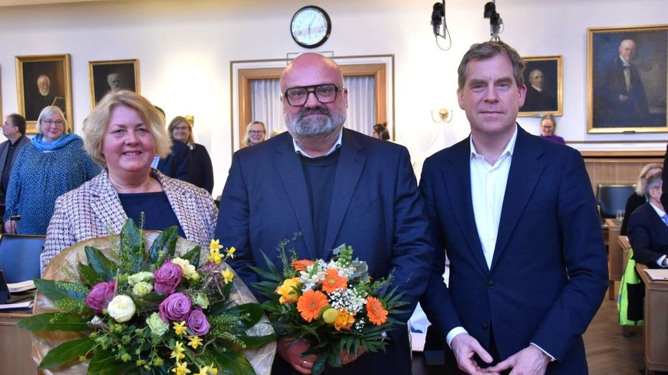 Drei Menschen im Kieler Rathaus, davon zwei mit Blumensträußen in der Hand
