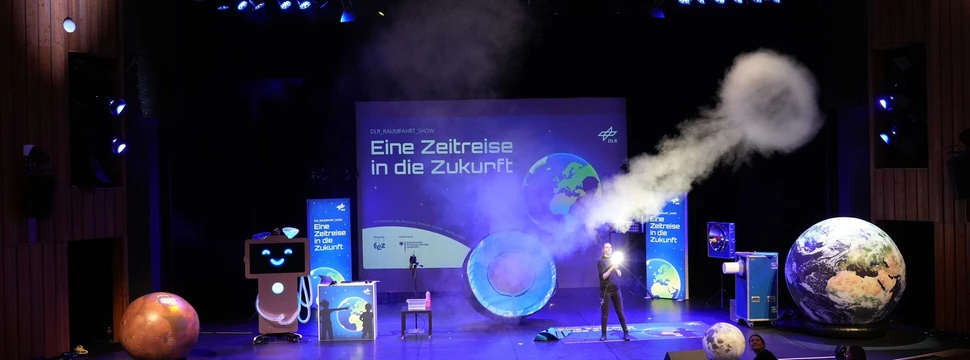 Ein Foto einer Bühnenshow mit dem Titel "Eine Zeitreise in die Zukunft" mit einem Menschen in der Mitte, der Experimente durchführt