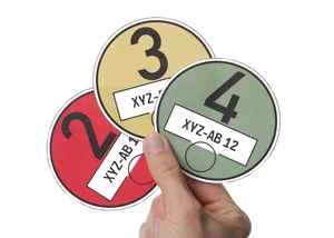 Eine Hand hält drei Umweltplaketten in unterschiedlichen Farben – rot, gelb und grün.