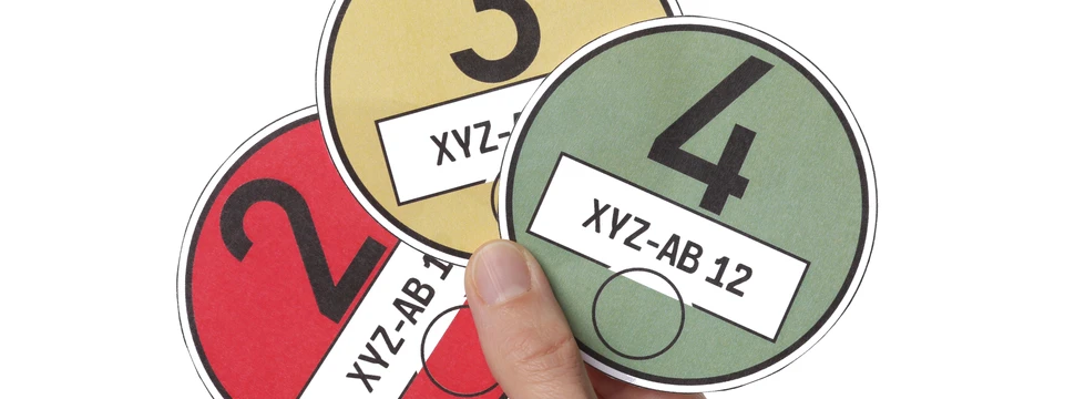 Eine Hand hält drei Umweltplaketten in unterschiedlichen Farben – rot, gelb und grün.