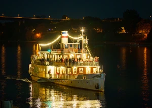 Schiff mit Lichterketten fährt durch eine Schleuse. Auf dem Schiff sind einige Menschen drauf