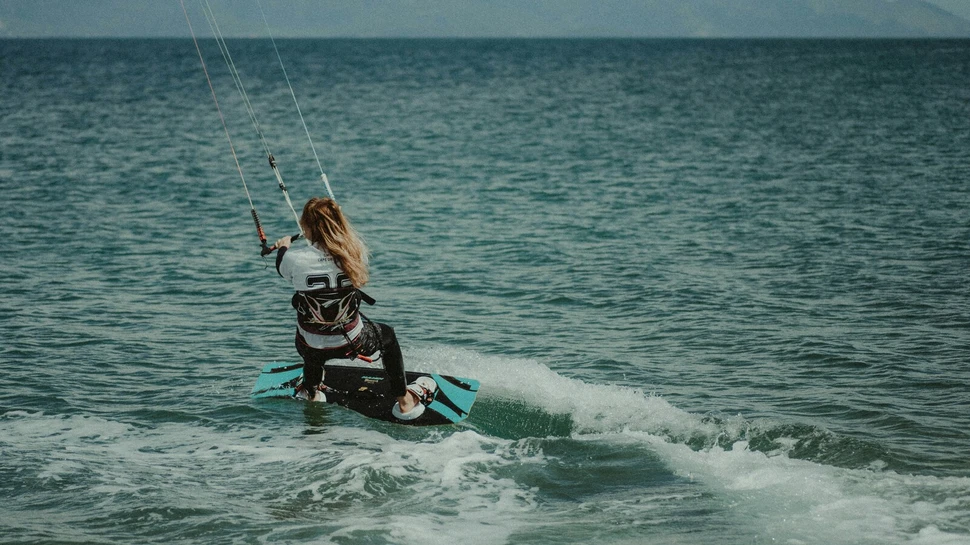 Frau ist auf einem Surfboard und wird von drei Seilen durch das Meer gezogen