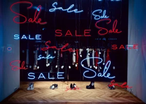 Neon-Schaufenster mit "Sale"-Angeboten in der Innenstadt. Schaufenster mit leuchtenden Neon-Schriftzügen "Sale" und ausgestellten Kleidungsstücken und Schuhen.
