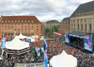 Mehrere Menschen vor einer Bühne auf dem Kieler Rathausplatz, auf der gerade ein Konzert läuft, das im Rahmen der Kieler Woche stattfindet
