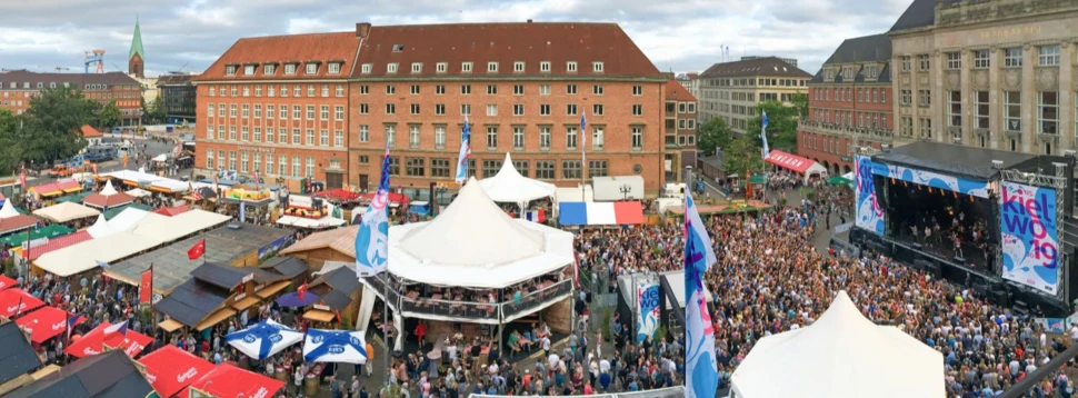 Mehrere Menschen vor einer Bühne auf dem Kieler Rathausplatz, auf der gerade ein Konzert läuft, das im Rahmen der Kieler Woche stattfindet