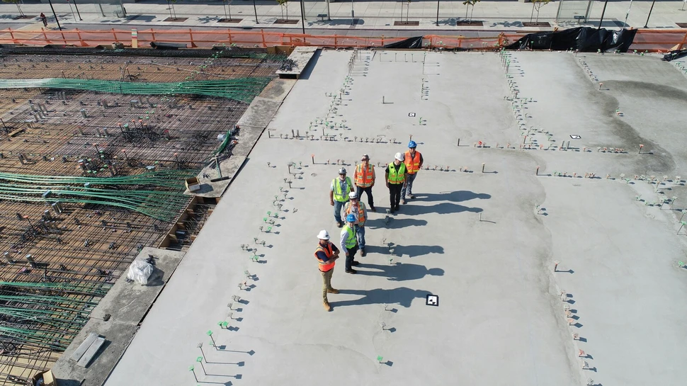 sieben Menschen steht auf einer großen Betonplatte. Sie befinden sich auf einer Baustelle.