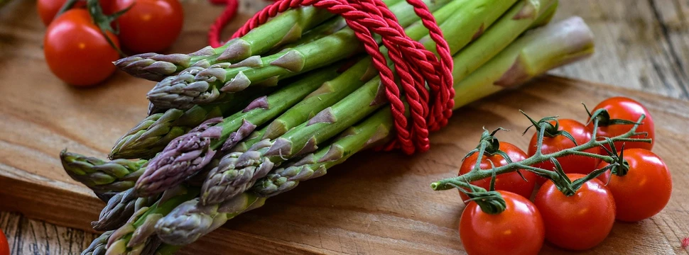 Grüner Spargel und Rispentomaten auf einem Holzbrett