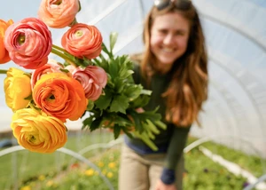 Frau hält einen Blumenstrauß, im Hintergrund sieht man ein Blumenfeld