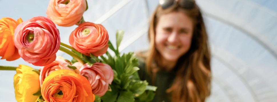 Frau hält einen Blumenstrauß, im Hintergrund sieht man ein Blumenfeld