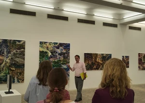 Ein Mann in einem rosa Hemd neben einigen Bildern in der Kieler Stadtgalerie, die Teil einer neuen Ausstellung sind