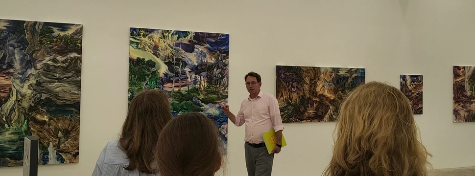 Ein Mann in einem rosa Hemd neben einigen Bildern in der Kieler Stadtgalerie, die Teil einer neuen Ausstellung sind