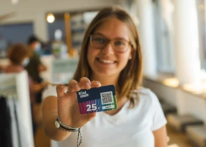 Junge Frau hält einen Kiel-Gutschein im Wert von 25 Euro lachend in die Kamera.