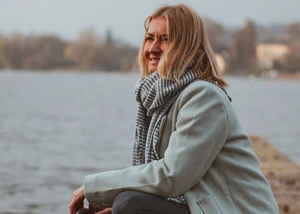 Frau im Wollmantel sitzt auf einem Steg