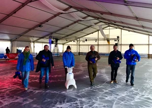 Eine Gruppe von sechs Personen mit Schneemann auf der überdachten Eisbahn. Sechs Menschen in Winterkleidung stehen mit einem kleinen Schneemann auf einer Eisbahn unter einem weißen Zelt.