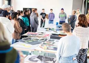 Mehrere Menschen an einem großen Tisch, auf dem Bilder liegen und die sich über einen neuen Studiengang informieren