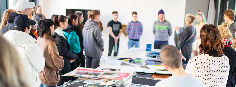 Mehrere Menschen an einem großen Tisch, auf dem Bilder liegen und die sich über einen neuen Studiengang informieren