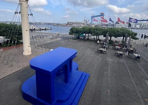 Ein blau gefärbtes Kunstprojekt vor der Kieler Förde mit den Werfttürmen von HDW im Hintergrund