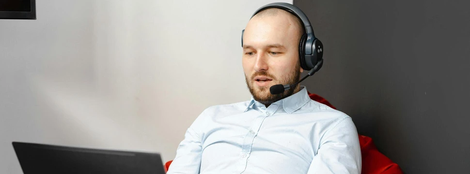 Ein Mann an einem Laptop, der ein Headset trägt und eine Besprechung an diesem Laptop durchführt