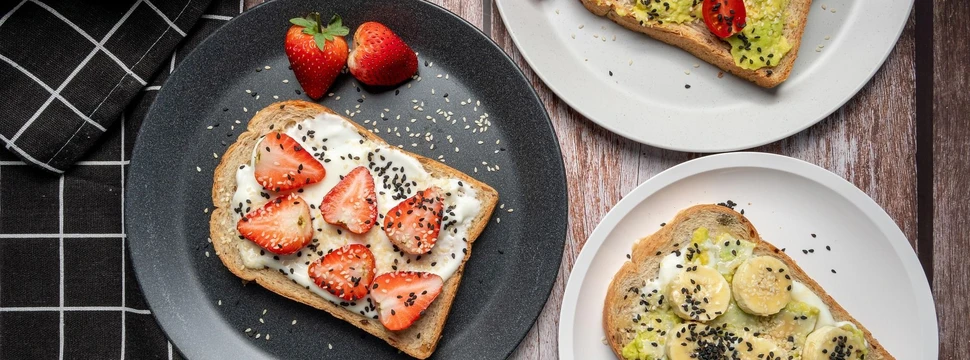 Ein schwarzer Teller, zwei weiße Teller jeweils mit frischen Früchten auf Toast