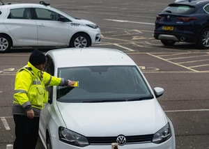 Ein Polizist an einem Auto, welches keinen gültigen Parkschein hat und deswegen ein Knöllchen bekommt