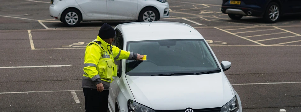 Ein Polizist an einem Auto, welches keinen gültigen Parkschein hat und deswegen ein Knöllchen bekommt
