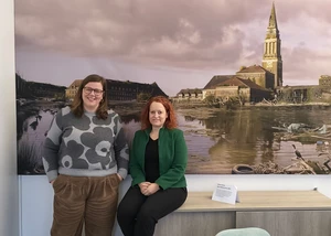 Zwei Frauen vor einem Bild, auf der das Kieler Rathaus mit einen übervollem kleinen Kiel zeigt