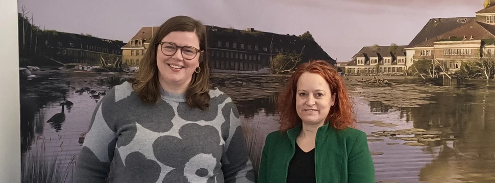 Zwei Frauen vor einem Bild, auf der das Kieler Rathaus mit einen übervollem kleinen Kiel zeigt