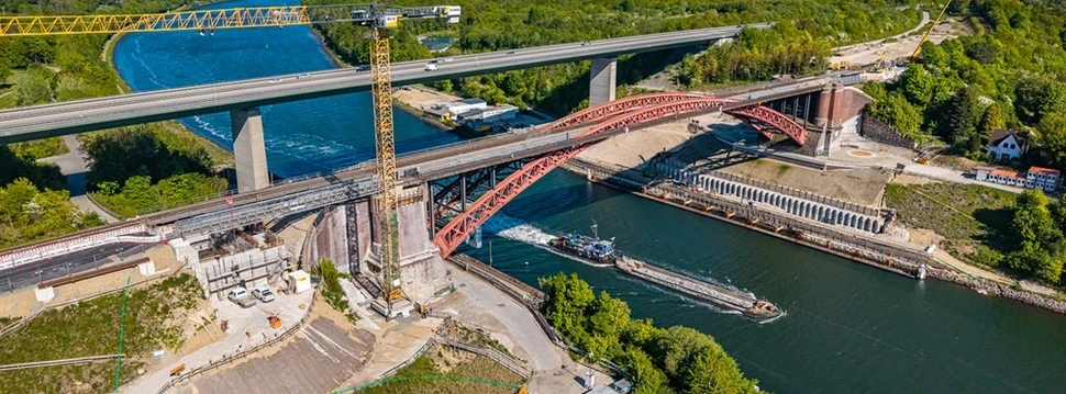 Zwei Brücken vor einem Kanal, an denen derzeit gebaut wird und unter denen gerade ein Schiff langfährt