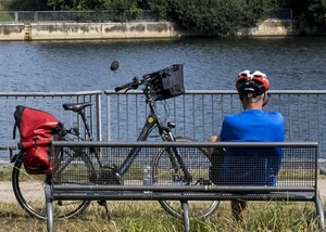 Ein Mensch auf einer Bank vor einem Fluss und einem Fahrrad neben sich