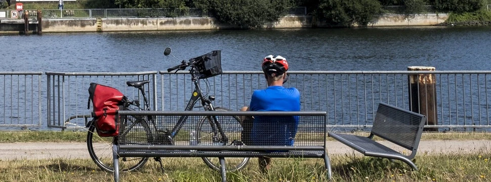 Ein Mensch auf einer Bank vor einem Fluss und einem Fahrrad neben sich