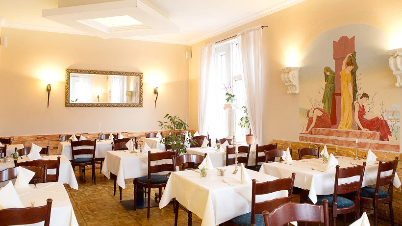 Das Restaurant Nostimo von Innen Ein Raum mit Lampen, braunen Holzstühlen und Tischen mit einer weißen Tischdecke
